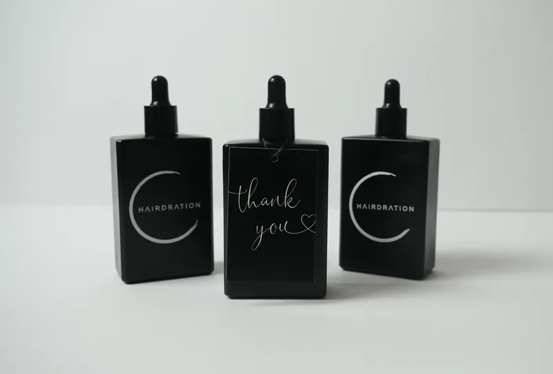 Three black Hairdration serum bottles with dropper caps, the middle one wrapped in a handwritten thank-you card