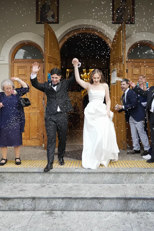 Newlyweds walking out of the church through falling confetti as guests cheer