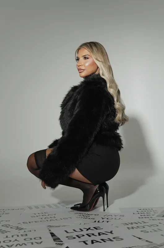 Bronz’d by Suzie founder crouching in a black faux-fur jacket on a studio backdrop