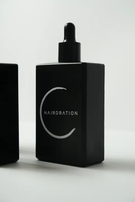 Close-up of a black Hairdration serum bottle with its crescent logo