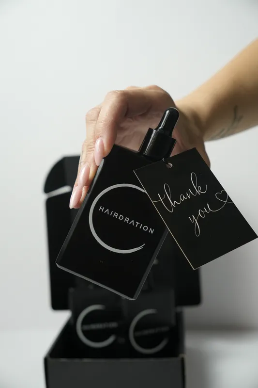 Hand lifting a Hairdration serum bottle with a thank-you tag out of its black box