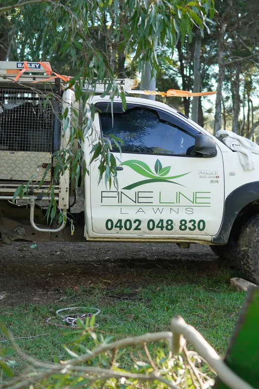 Fineline Lawns ute with the company logo and phone number parked under trees