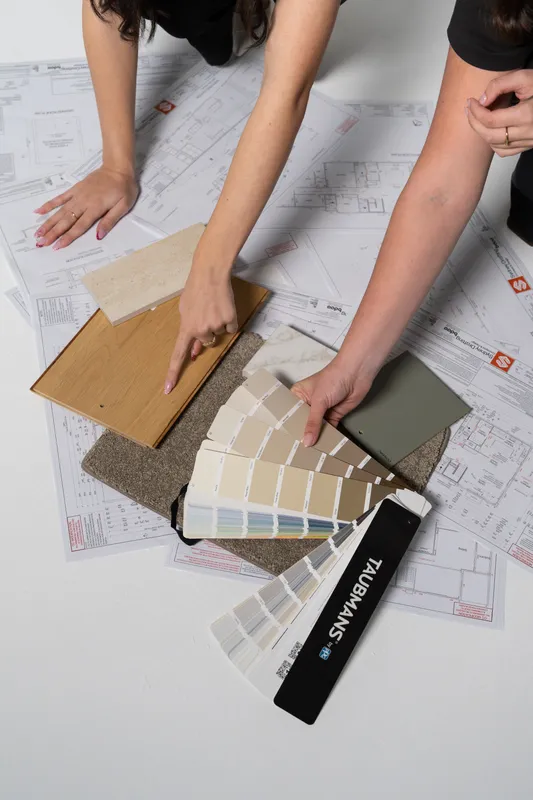 Hands choosing timber, carpet and paint samples on top of building plans