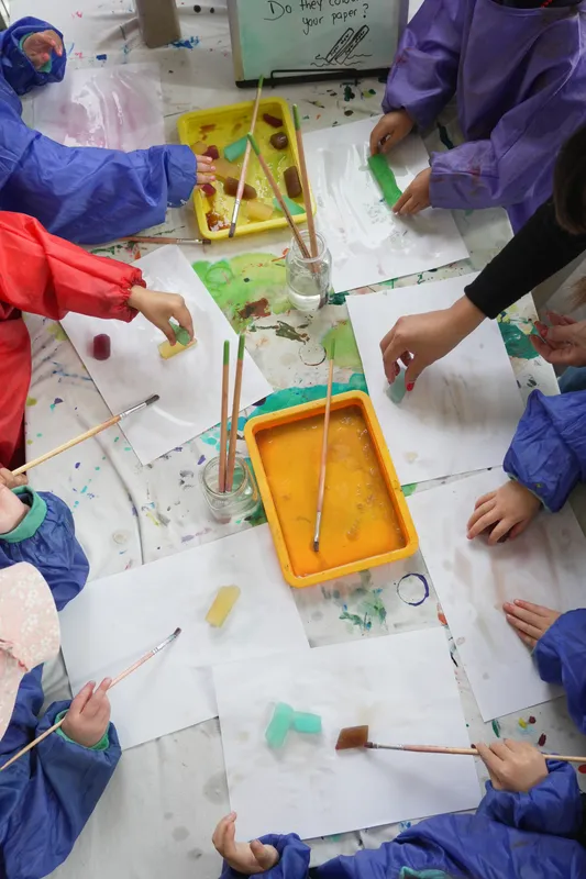 Children in smocks painting with brushes around a big sheet of paper at Woodstock Early Learning Centre