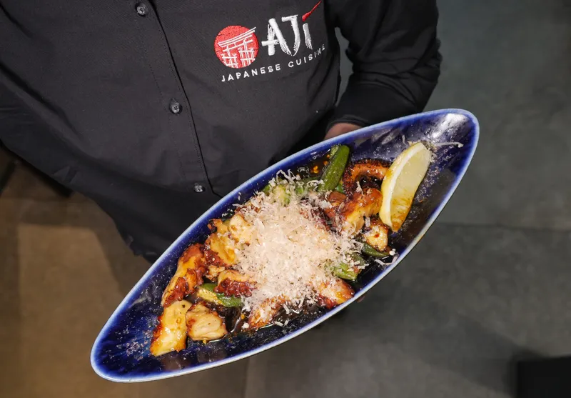 Aji Japanese Cuisine chef holding a long blue plate of grilled eel topped with bonito flakes