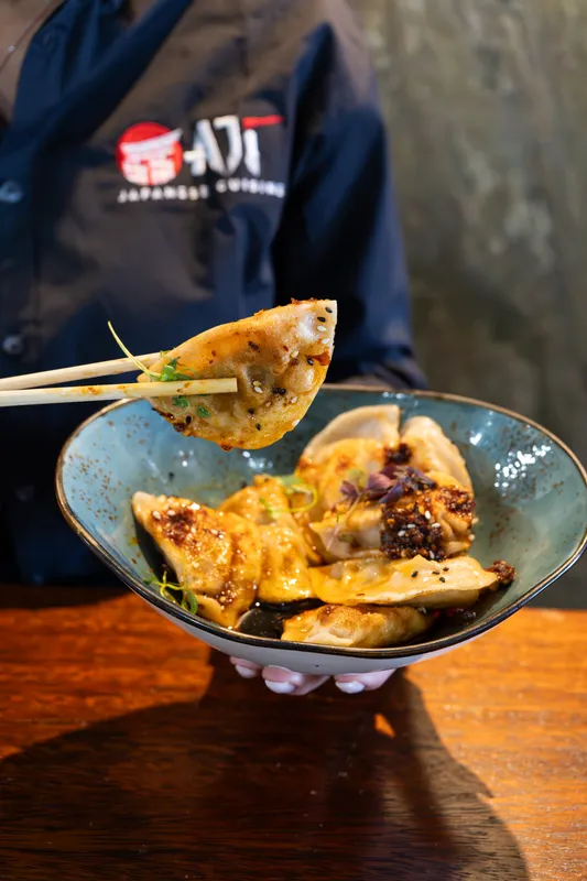 Chopsticks lifting a gyoza from a blue bowl at Aji Japanese Cuisine
