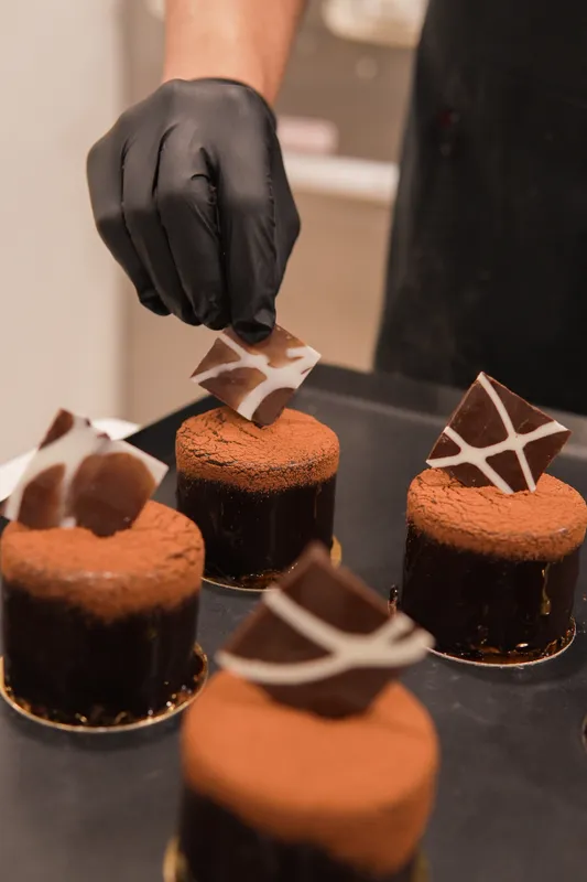Gloved hand placing chocolate shards on chocolate mousse cakes at Galerie Pâtisserie