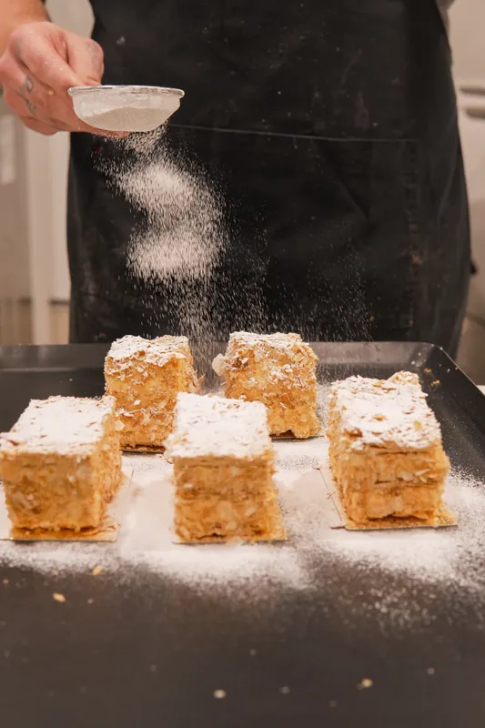 Dusting icing sugar over vanilla slices at Galerie Pâtisserie