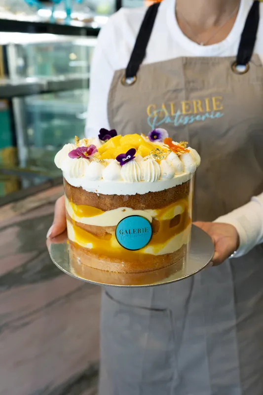 Galerie Pâtisserie staff member holding a layered cake topped with cream and edible flowers
