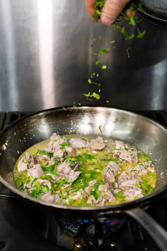 Chef sprinkling fresh herbs into a pan of meat at Gebran Lebanese Cuisine