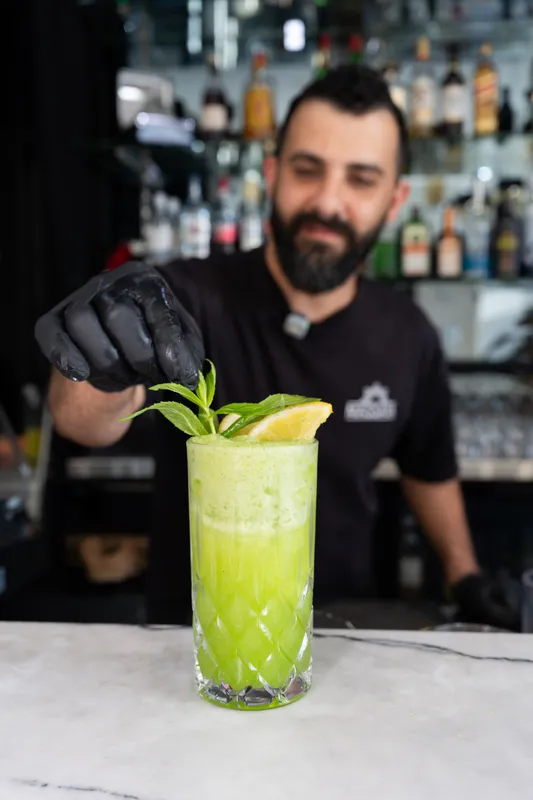 Gebran bartender garnishing a bright green cocktail with mint