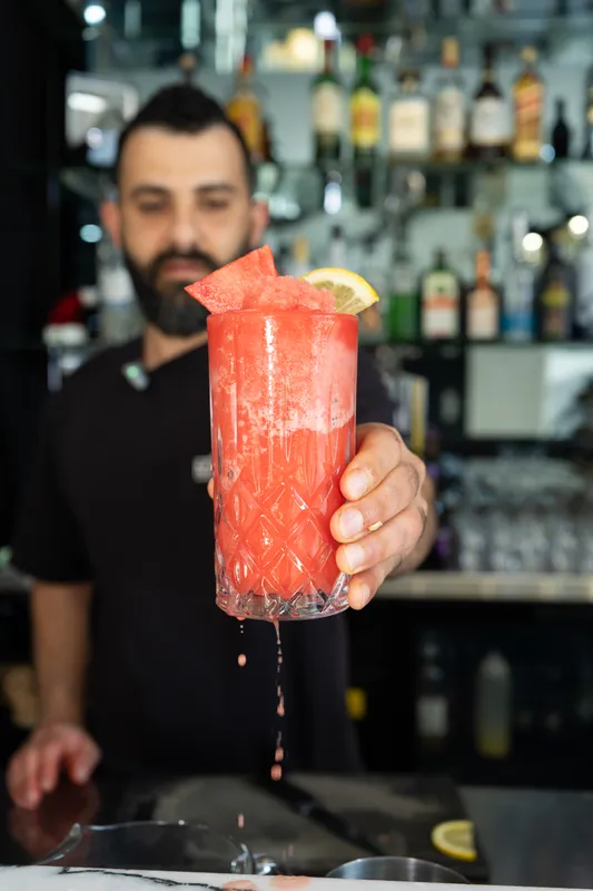 Gebran bartender holding up a red frozen cocktail at the bar