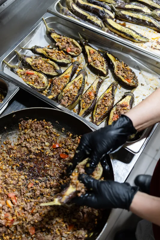 Gloved hands filling roasted eggplants with spiced mince at Massaya