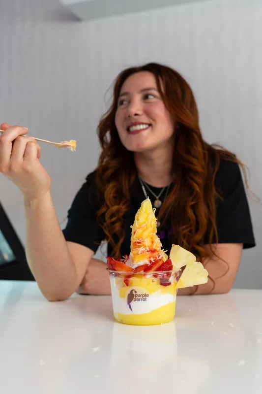 Woman smiling as she eats a Purple Parrot pineapple soft-serve sundae