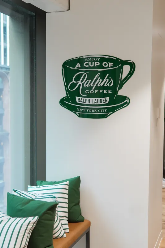 Green “A cup of Ralph’s Coffee” sign above striped cushions at Ralph’s Coffee