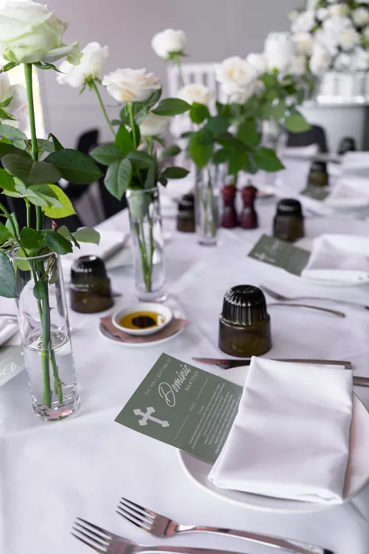 Christening table setting with white roses, green menu cards and white napkins