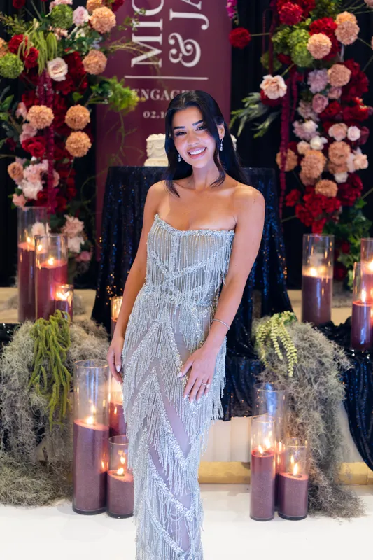 Bride-to-be in a beaded silver gown in front of a candlelit floral engagement backdrop