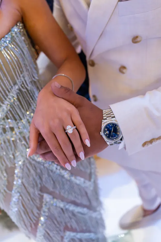 Close-up of the couple’s hands showing the engagement ring against a beaded silver dress