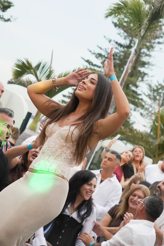 Woman in a white dress dancing with her arms raised among guests at an outdoor celebration