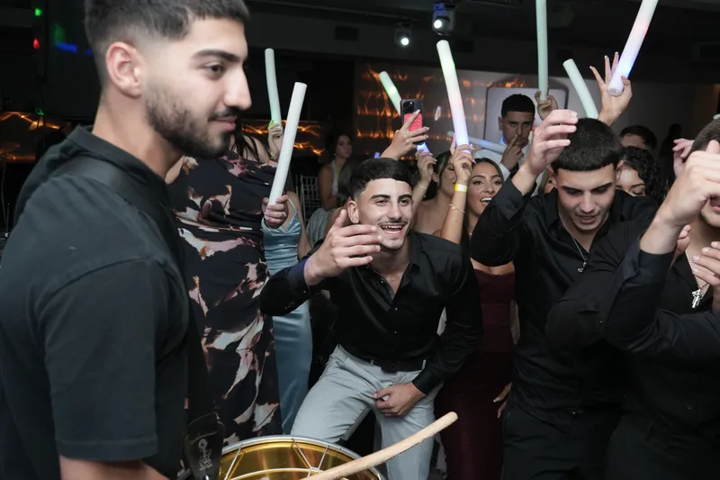 Young men singing and holding glow sticks on a crowded dance floor