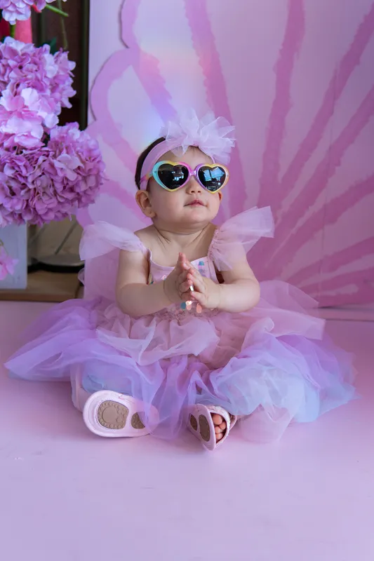 Baby girl in a purple tutu and heart sunglasses at her first birthday