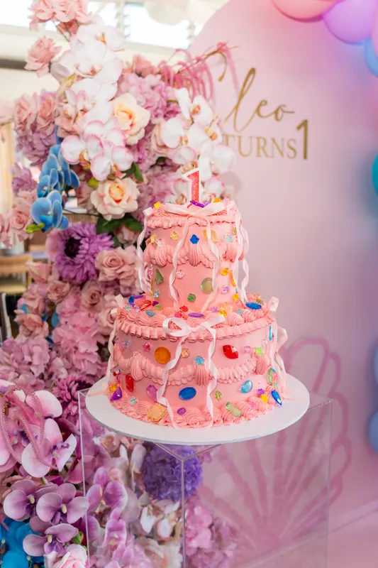 Colourful first-birthday cake with a flower display and a pink backdrop
