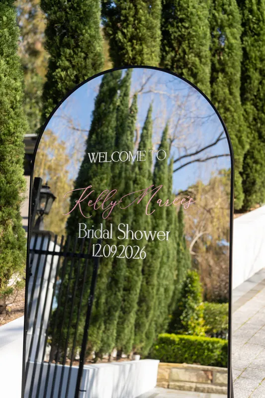 Bridal shower welcome sign in a black arch between tall cypress trees