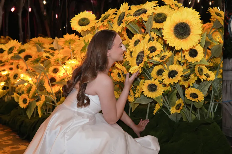 Bride in her gown leaning towards a wall of sunflowers