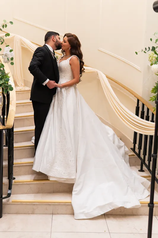 Bride and groom embracing at the foot of a white curved staircase