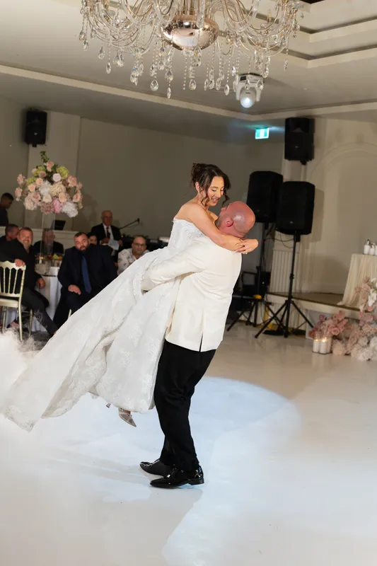 Groom lifting and spinning his bride on the dance floor under chandeliers