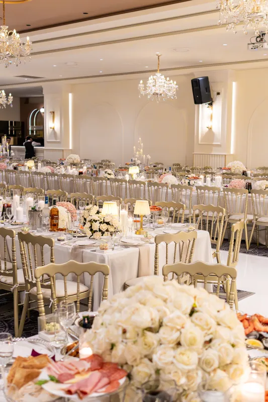 Wedding reception hall with long tables, white roses and crystal chandeliers