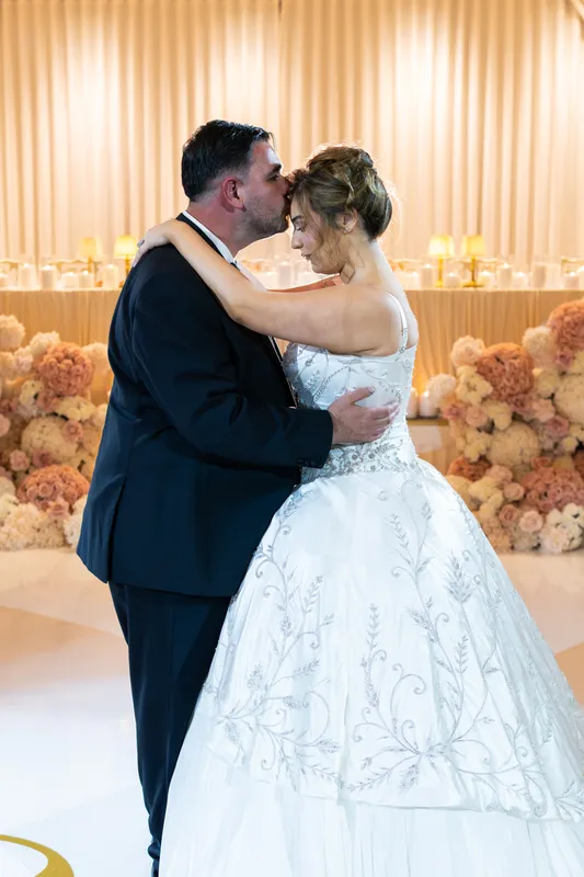 Bride and groom slow dancing in front of the bridal table and peach flowers