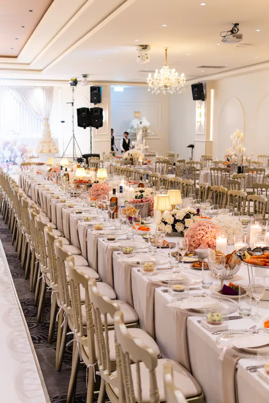 Long reception tables set with gold chairs, candles and flowers in a ballroom
