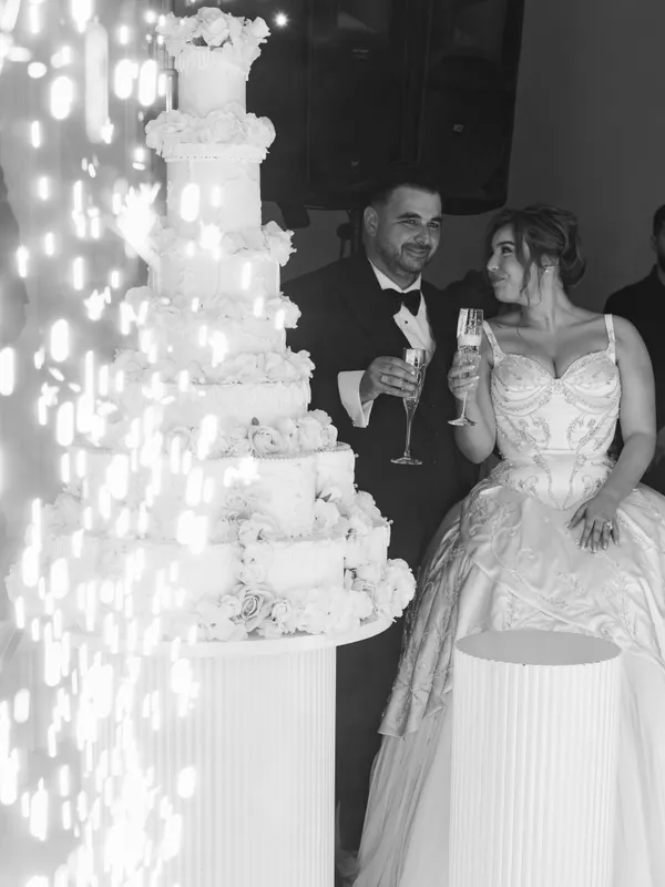 Black-and-white photo of the newlyweds raising glasses beside a tall cake and sparklers